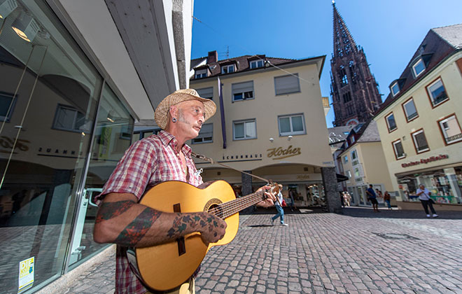 Straßenmusiker mit Gitarre in einer Fußgängerzone.