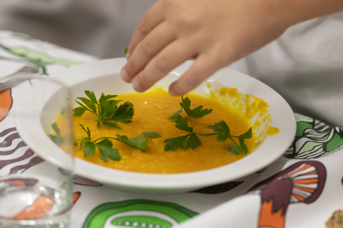 Teller mit Kürbissuppe, auf die eine Kinderhand gerade Koriander streut