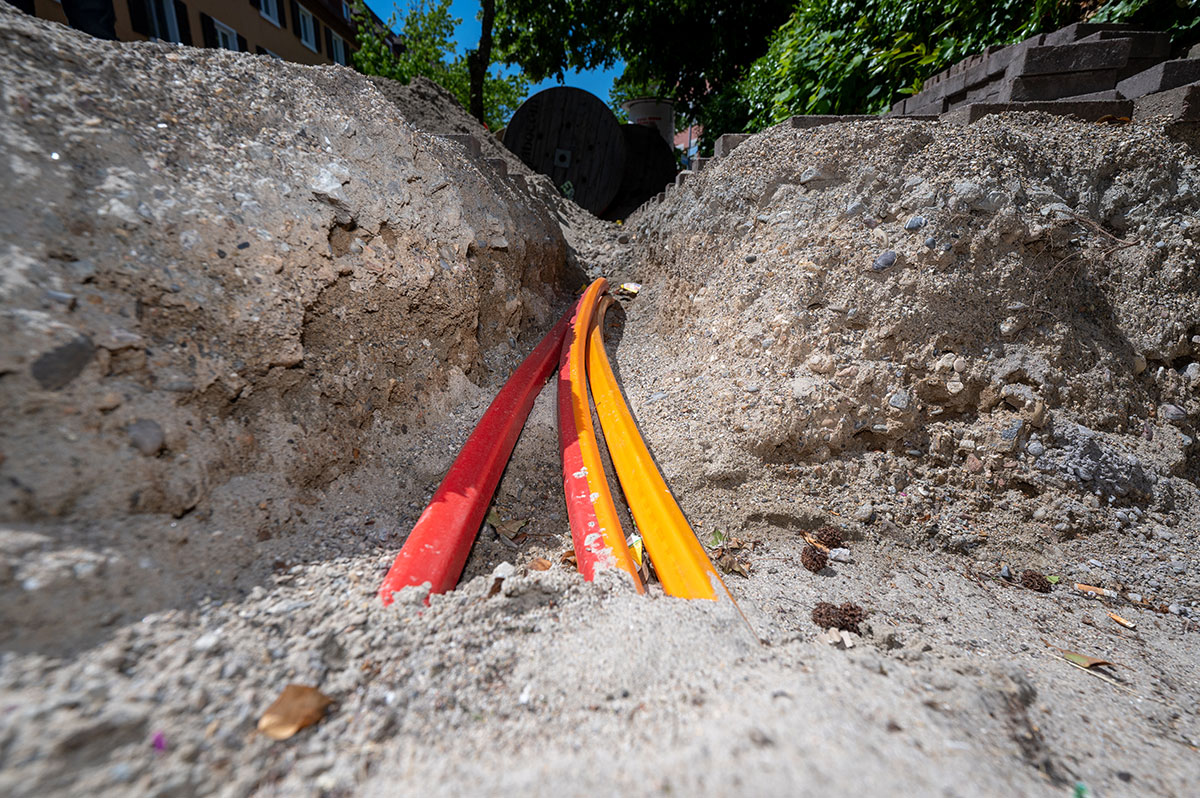 Drei rot-gelbe Leerrohre ragen aus einer Glasfaserbaustelle aus der Erde