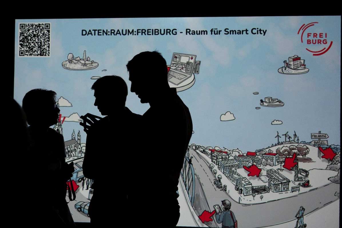 3 Personen vor einer Leinwand mit Datenraum-Präsentation