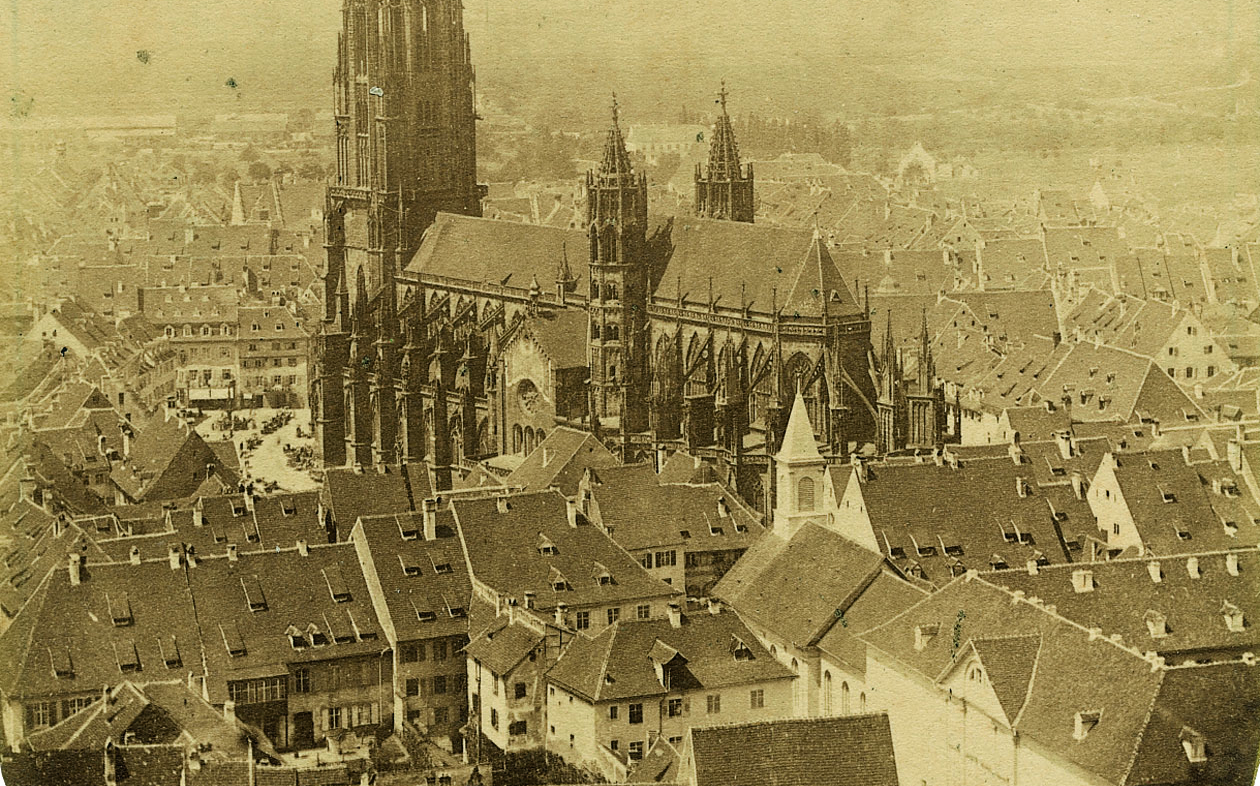 Eine alte Sepia-Fotografie vom Stadtzentrum Freiburgs in der Mitte des 19. Jahrhunderts, aufgenommen von Gottlieb Theodor Hase vom Schlossberg. Im Zentrum des Bildes befindet sich das Freiburger Münster.