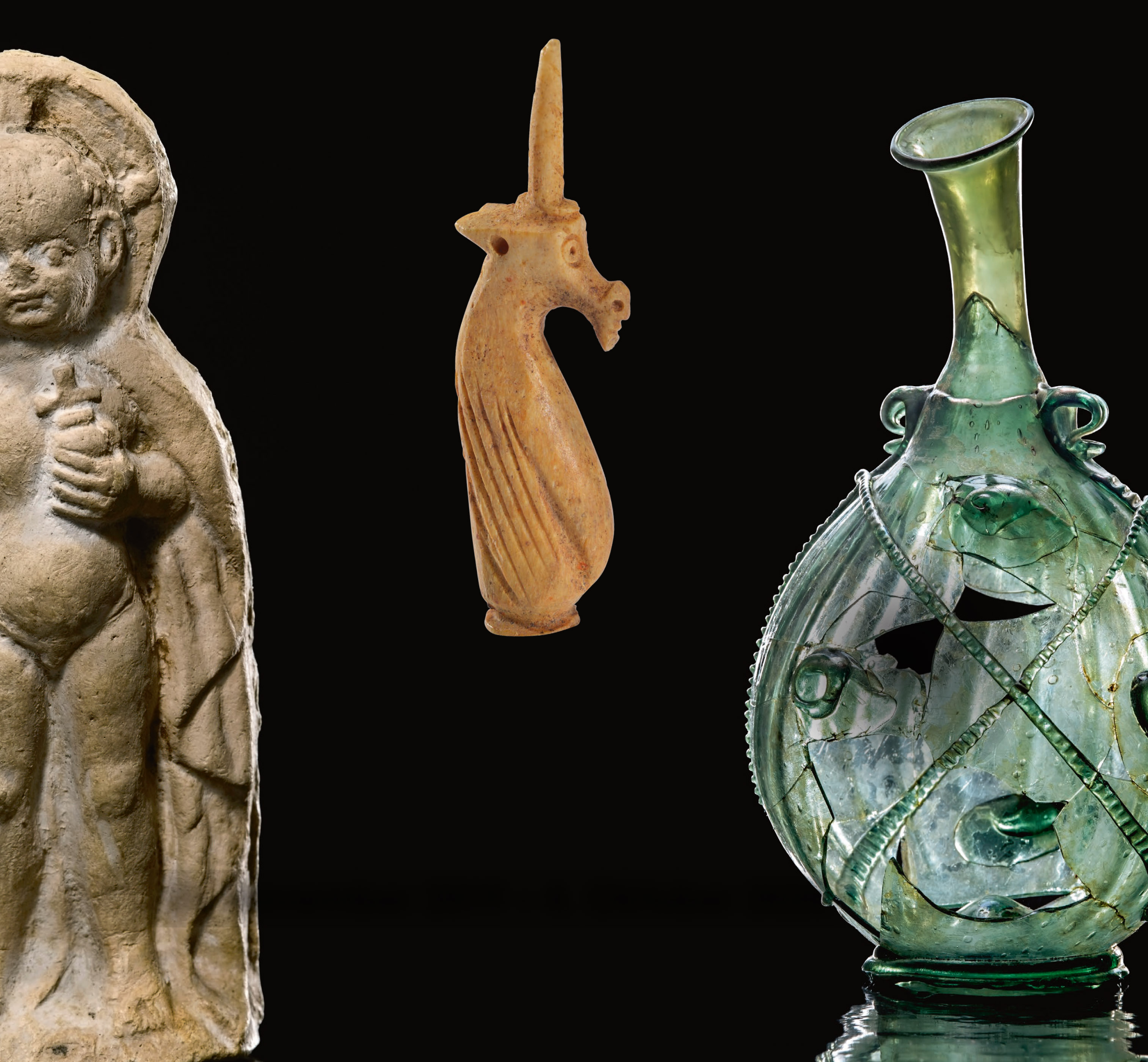 3 archäologische Objekte auf schwarzem Hintergrund: ein Jesusknabe, ein Einhorn und eine gläserne Vase.