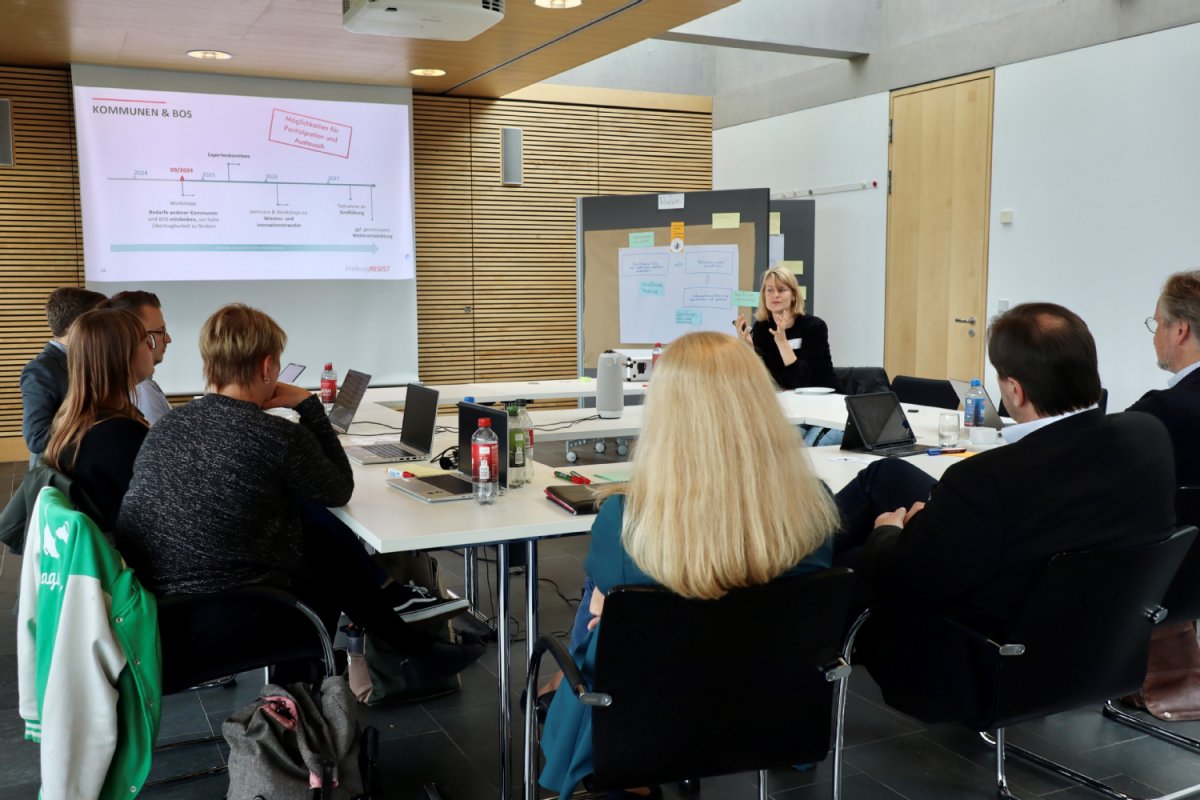 Menschen sitzen an einem Tisch und schauen sich eine Präsentation auf einem Beamer an.