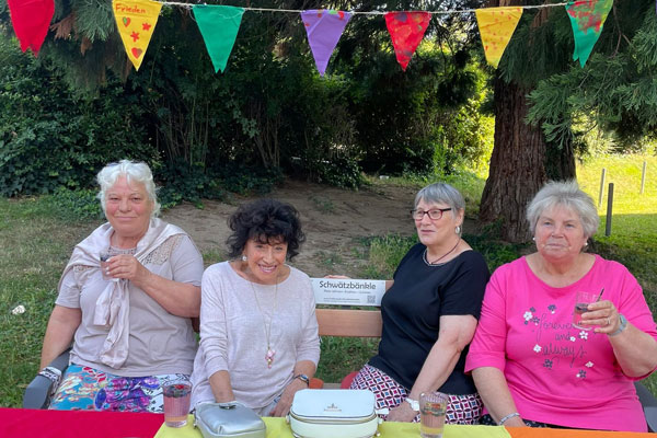 Vier ältere Damen auf einer Bank, darüber bunte Wimpel
