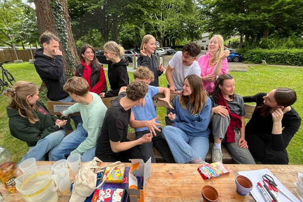 Viele Jugendliche sitzen auf dem Schwätzbänkle und unterhalten sich. Auf dem Tisch sind Getränke, Essen und Spiele