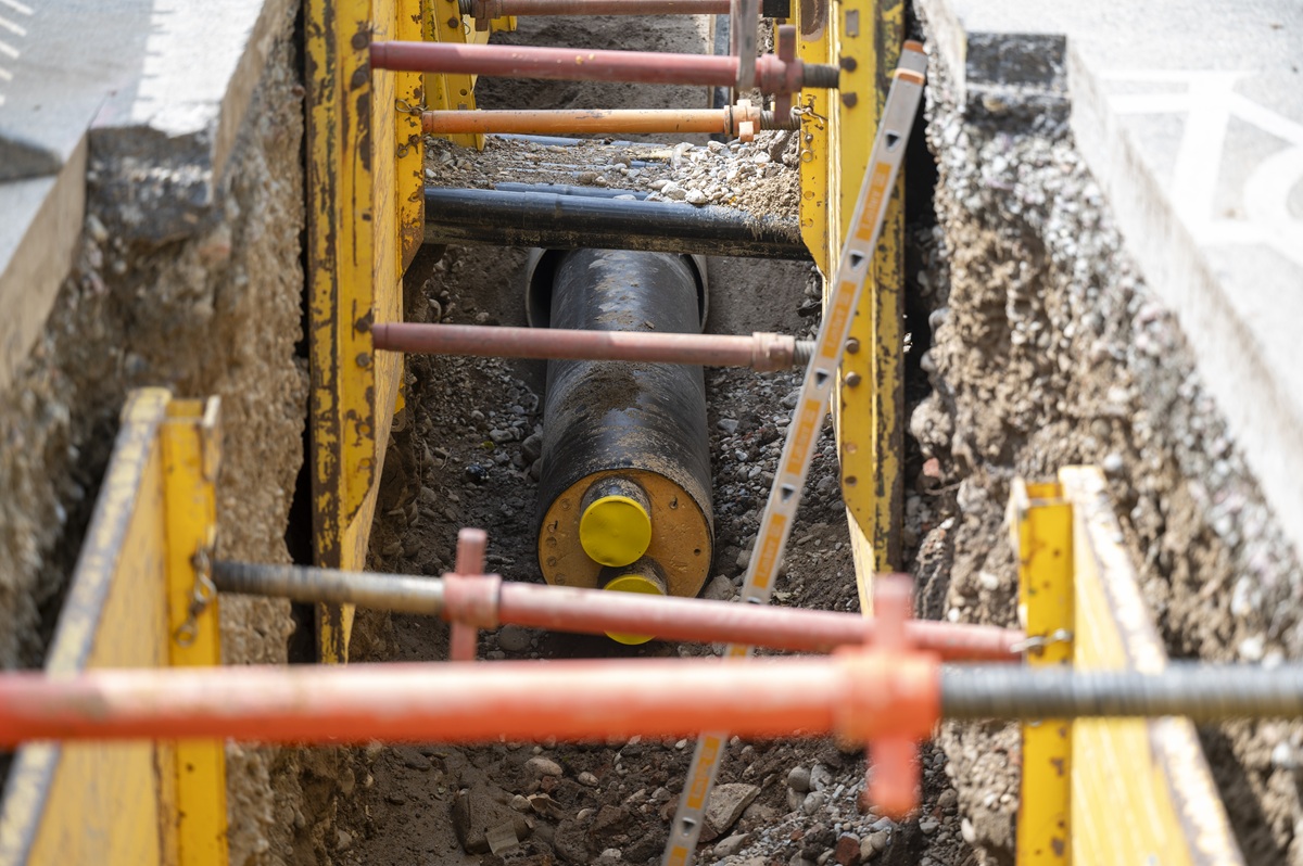 Ein Fernwärmerohr liegt unter der Erde, die Straße ist aufgebrochen und es sind Stützen angebracht.
