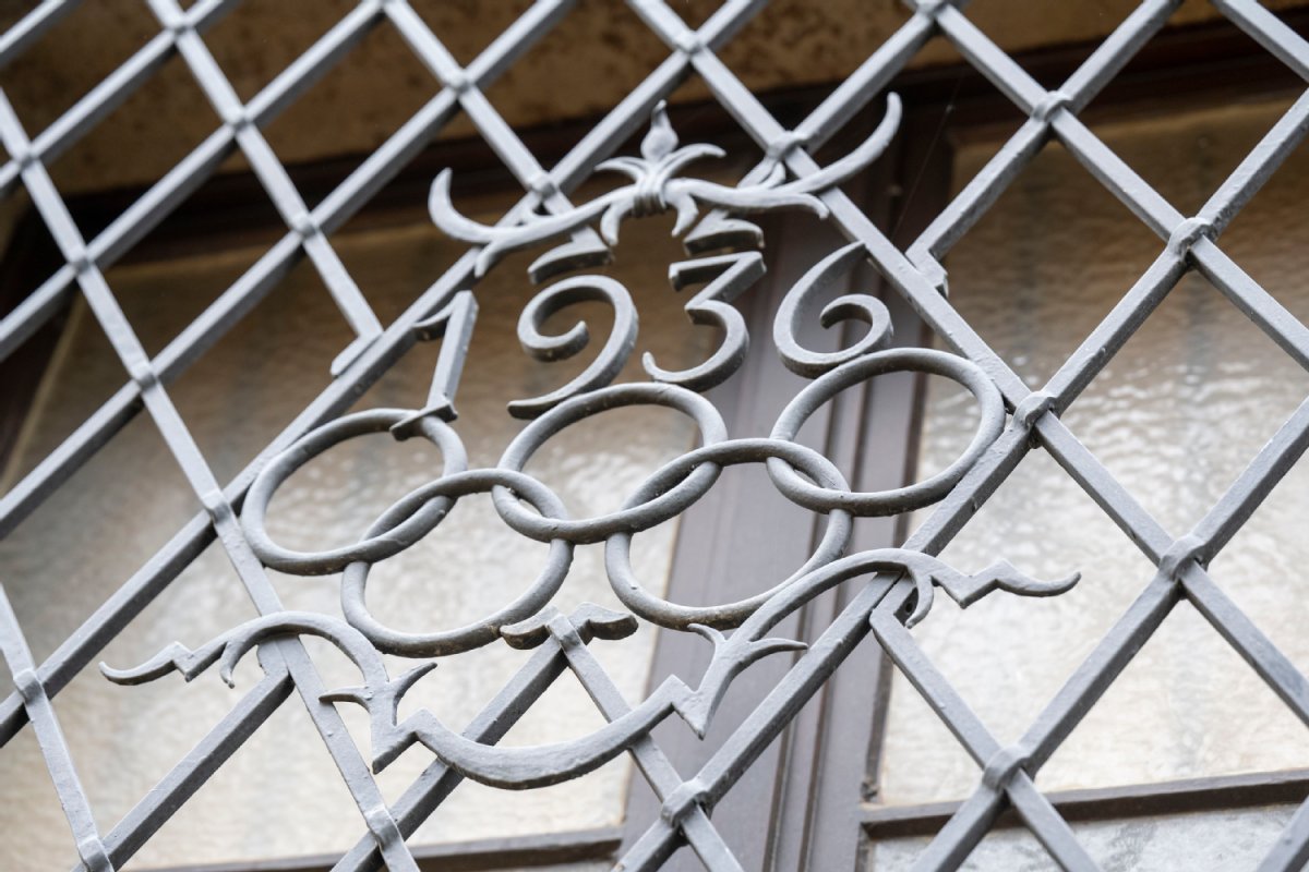 Karierter Metallzaun, in der Mitte die Jahreszahl 1936 und darunter die olympischen Ringe