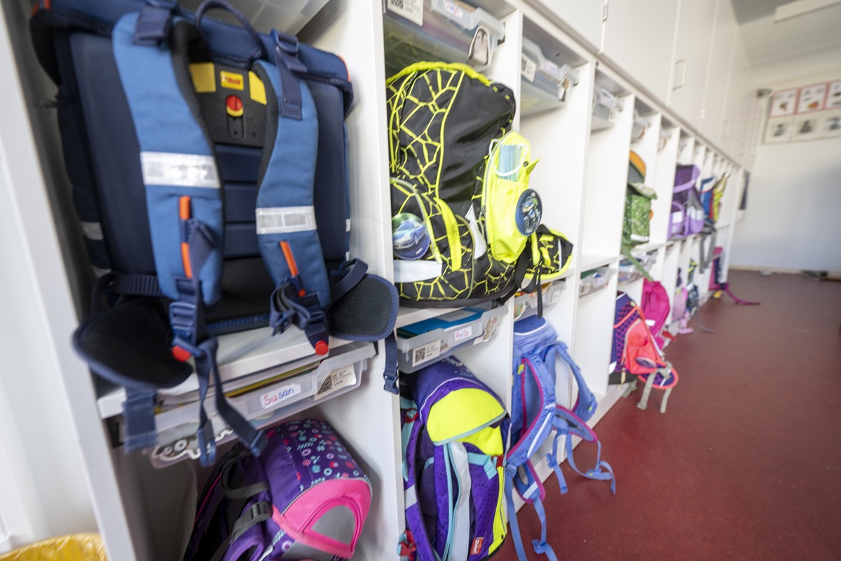 Bunte Schulränzen stehen ordentlich in einem weißen Regal.